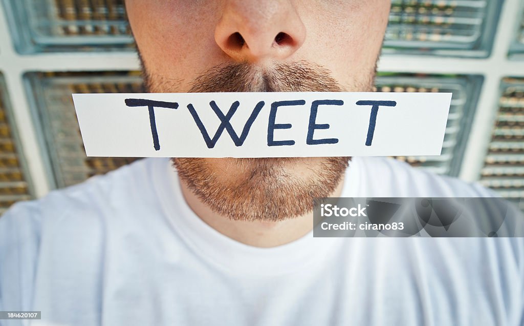 Man With Adhesive Note Tweet On The Mouth Man with adhesive note with word Tweet on the mouth. Focus on Tweet. Adhesive Note Stock Photo