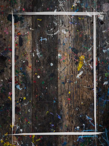istock White brush stroke frame on wood plank top table covered in color paint splatter, vertical style. Abstract texture rustic wooden desk background of artist studio with messy colorful painted splash. 1846223217