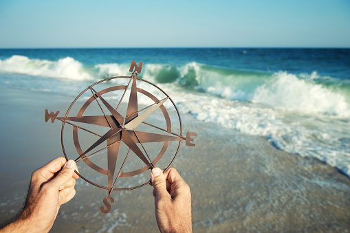 Hands holding compass above a scene of crashing waves blue sea