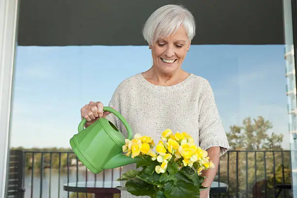 Senior lady taking care of her yellow flowers on balcony.