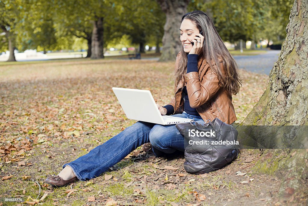 Молодая женщина, используя ноутбук и смартфон в парк - Стоковые фото 20-29 лет роялти-фри