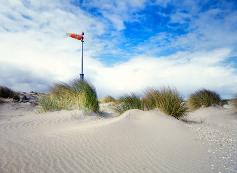 low angle view on a windsock standing on top of dunes and marram grass at a cloudy sky