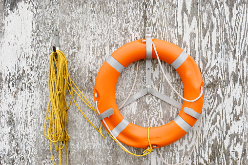 Orange lifebuoy and rope hanging on a weathered gray wooden wall.