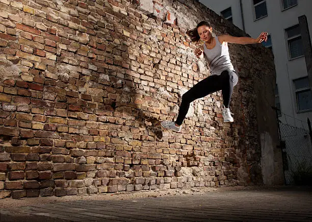 Young woman Tic-Tacing off a wall to change direction while doing Free-Running/Parkour in an urban area. Horizontal shot.