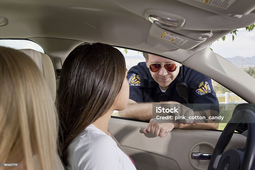 Young Woman Pulled Over by Police Young women in car talking to police officer who pulled her over. Focus on officer's face. Discussion Stock Photo