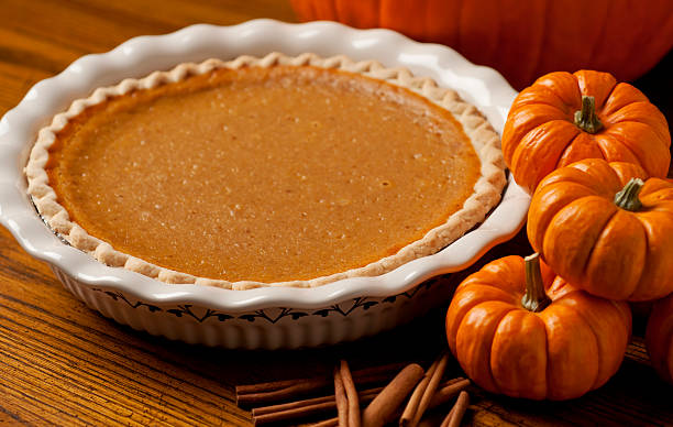 Pumpkin pie in white dish beside three pumpkins