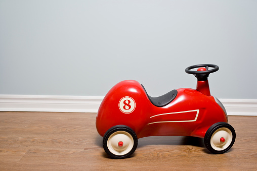 Little red toy car sits on brown hardwood floor in a home showing the concept of childhood, toys, and imaginative play