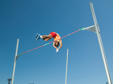 Pole Vault Jumping: Professional Male Athlete on World Championship Successfully Jumping with Pole over Bar. Shot of Competition on Big Stadium with Sports Achievement Experience