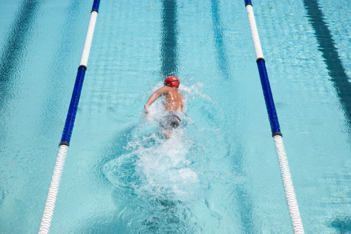 A young female swimmer is jumping of starting block into the swimming pool.