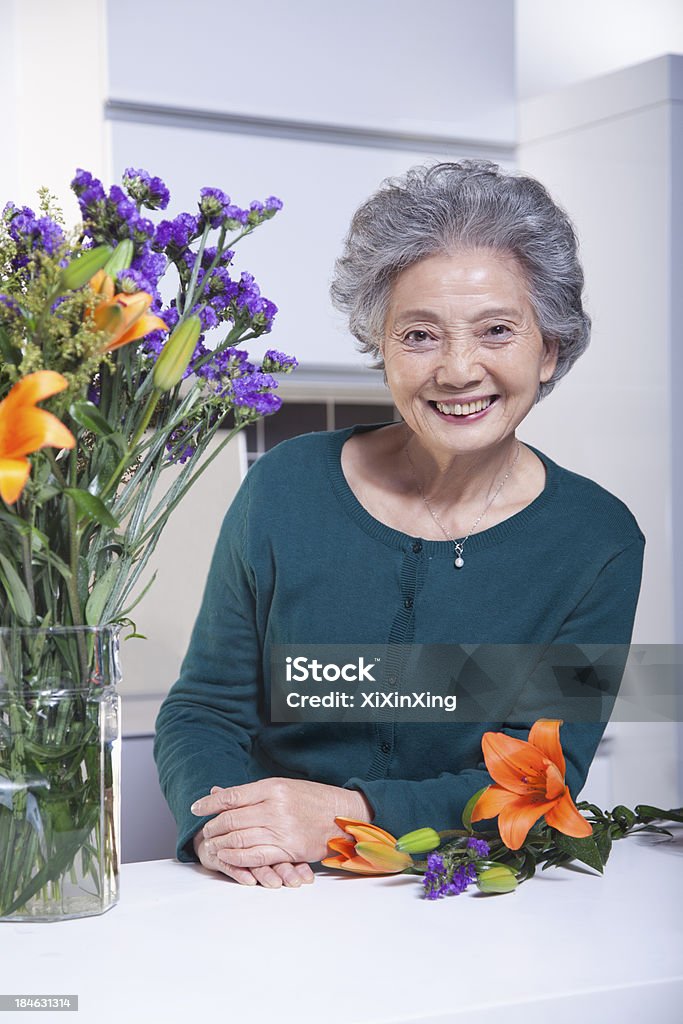 Starszy kobieta obok bukiet kwiatów w kuchni, Portret - Zbiór zdjęć royalty-free (Rozpinany sweter)