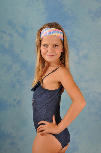 Slim pretty girl eight years in swimsuit portrait on blue background looking at camera