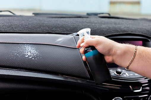Close-Up of a man's hand spraying a cleaning solution on the car interior.
