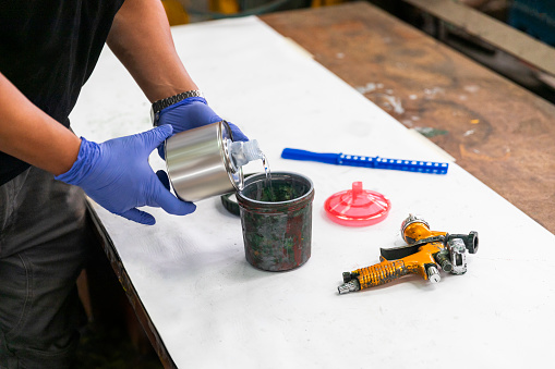 Man pouring liquid into a paint tin, preparing for a painting or renovation project.