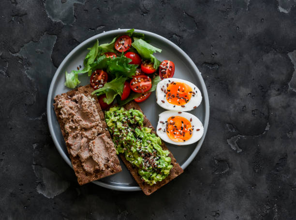 Delicious breakfast, tapas, snack - crispy rye bread with turkey liver, avocado, boiled egg and vegetable salad on a dark background, top view Delicious breakfast, tapas, snack - crispy rye bread with turkey liver, avocado, boiled egg and vegetable salad on a dark background, top view egg cherry tomato rye stock pictures, royalty-free photos & images