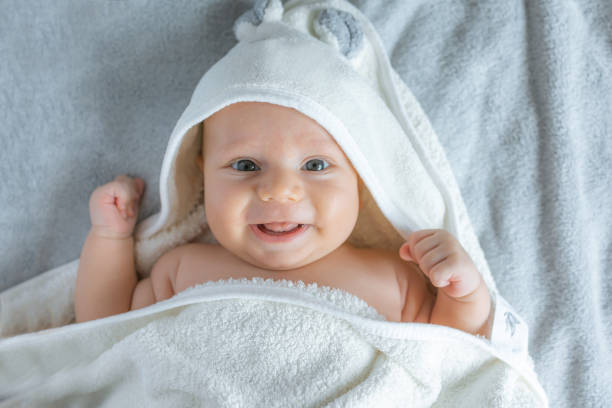 Cute infant baby in white hood bathrobe on changing table after bath.