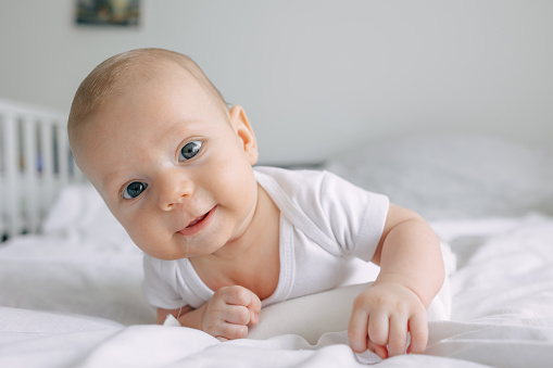 Closeup portrait of adorable infant baby boy lying on white blanket on stomach, smiling. Concept of children, baby, parenthood, childhood, life, maternity, motherhood