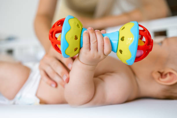 赤ちゃんは抱っこして、ガラガラと遊ぶ。細かい運動能力、視覚、聴覚を発達させるためのおもちゃ。 - auditory cortex ストックフォトと画像