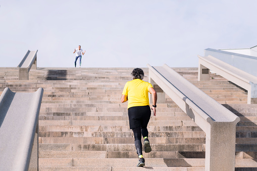 rear view of an unrecognizable sports senior man training on stairs while receiving encouragement from personal trainer, concept of active and healthy lifestyle in middle age, copy space for text