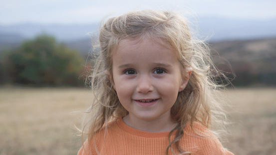 close-up of a smiley little girl in pink coat on green grass meadow