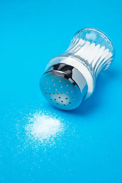 Spilled salt and saltshaker on blue background