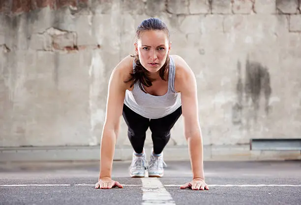 "Young woman with intense look, in step three the pushup postion of  Burpee exercise. Horizontal shot."