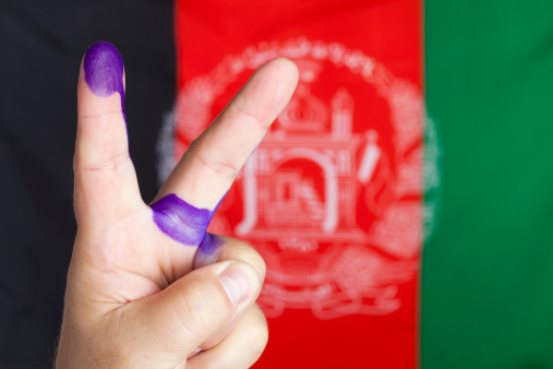 Man showing finger of his left hand stained with electoral stained. Technique used in Afghanistan and some other countries in order to prevent double voting.  The flag of Afghansiatn in the background. Selective focus.