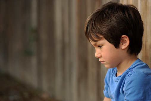 upset boy leaning against a wooding fence