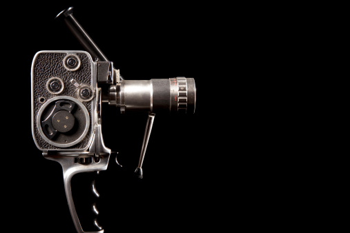 A close up of a vintage movie camera with a zoom lens on black.