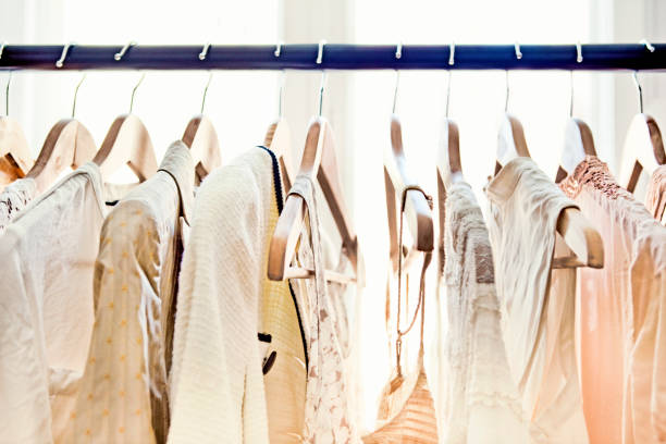 Hangers with clothes A row of light-colored clothing secured on wooden hangers is visible from about armpit level up, dangling from a rod which stretches from one end of the frame to the other.  Behind the rack, two large windows brighten the room with daylight. coathanger photos stock pictures, royalty-free photos & images