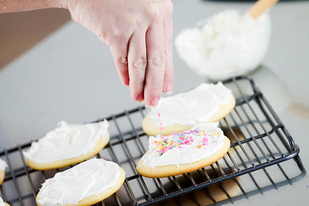 Decorating Holiday Cookies A woman decorating sugar cookies with frosting and sprinkles. round sugar cookie stock pictures, royalty-free photos & images