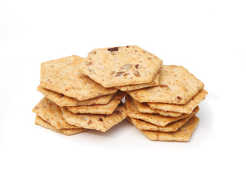 This is a macro studio shot of a stack of small crackers made with wheat and chopped toasted pecans. This is a studio shot on a white background.