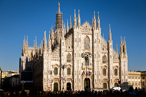 Duomo di Milano, the famous cathedral of Milan in late summer against blue cloudless sky. Late afternoon light with unrecognizable tourists in the shadow at Piazza del Duomo. Milan, Italy.