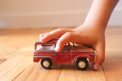 This image is of a young boy stopping the forward motion of an antique toy SUV while playing on the floor.