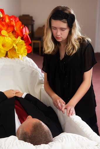 A young girl mourning over the death of a man at a funeral home.