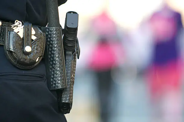 "Police officer's pistol, baton and handcuffs on a gun belt while monitoring a public event."
