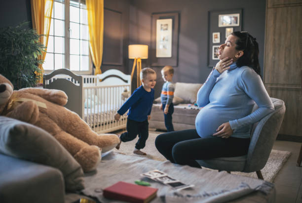 Une jeune femme enceinte souffre pendant que ses enfants jouent dans la pièce - Photo