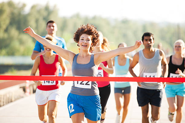 Group of runners in a cross country race. A young female runner tearing finishing tape. end of the line stock pictures, royalty-free photos & images