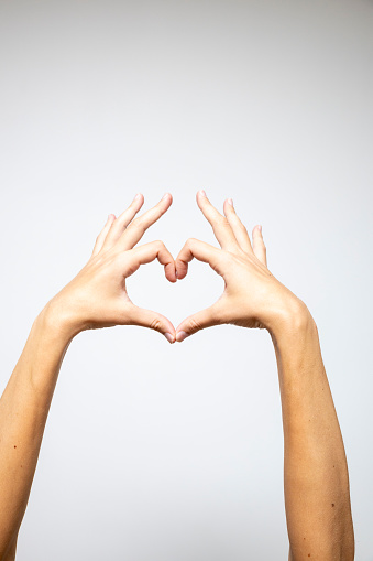 Two hands delicately intertwined to form a heart shape against a clean white background.