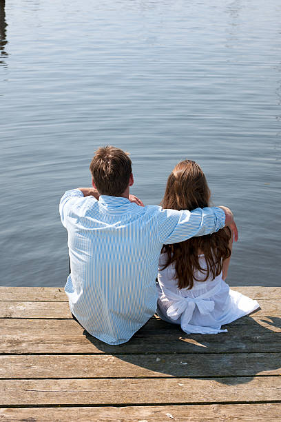 istock embracing couple sitting on pier at waterfront 184646454