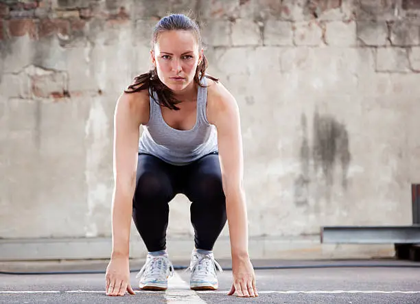 "Young woman with intense look, in step two the squat postion of  Burpee exercise. Horizontal shot."