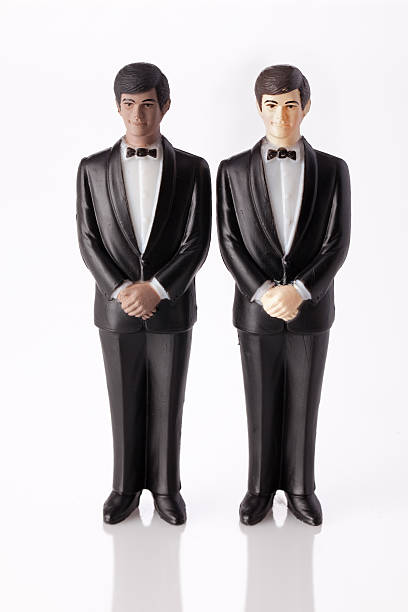 This is a close-up of a small, painted figurine showing a bride and groom sitting on a red, heart-shaped chair. The paint on the figurine appears worn and chipped, giving it a vintage look.