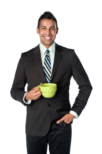 Young and hip Indian businessman in a suit jacket and black jeans holding a green coffee mug.