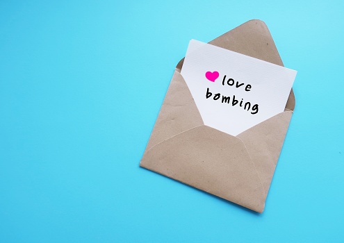 Envelope with card on blue background with text written LOVE BOMBING, extreme romantic attention offered intensely too much too fast to influence feelings or tactic used by narcissists to control partners