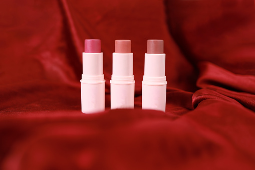 Lipstick on bright scarlet silk or maroon fabric background with soft folds, realistic cosmetic. Beauty Product.