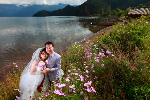 picture of happy asian couple looking at camera smile. pretty bride holding flowers.