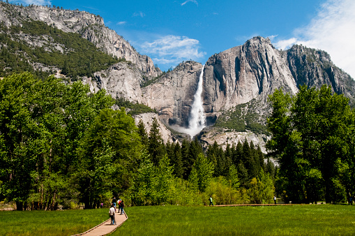 View from the road of Yosemite Waterfall. Unrecognisable people walking along the path in-front of it.