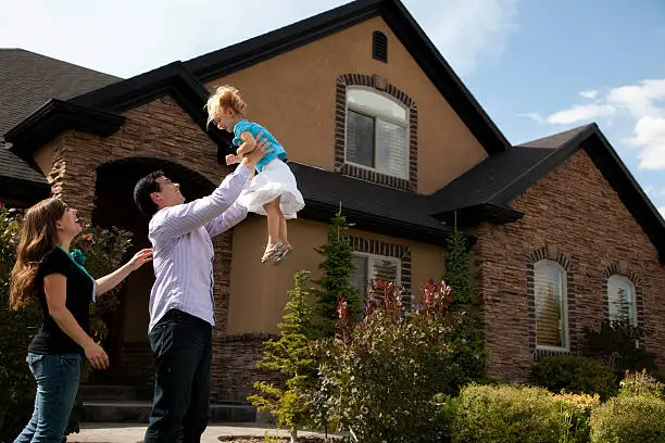 "Cute young couple celebrates and has fun in front of their beautiful home.  Dad tosses child into the air playfully.Shot with Canon 5D Mark II, image processed in Pro Photo from a 16 bit RAW file.  Slight color saturation added."