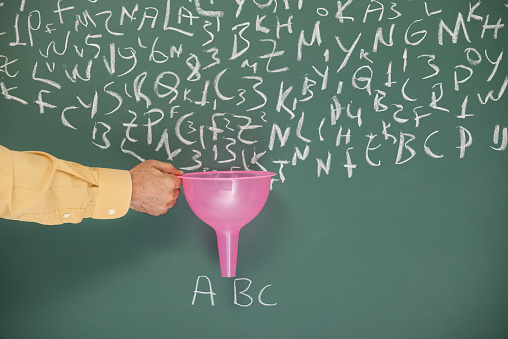 A funnel in hand of man filtering letters written on blackboard by chalk.Search engine optimization -SEO- concept is aimed.The hand is on the left side of the horizontal frame.The funnel pink color is for having attention on filtering. The letters 
