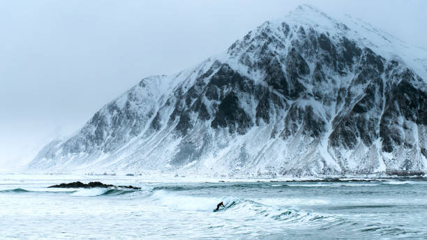Surfer in wetsuit riding surfboard on small wave in ocean