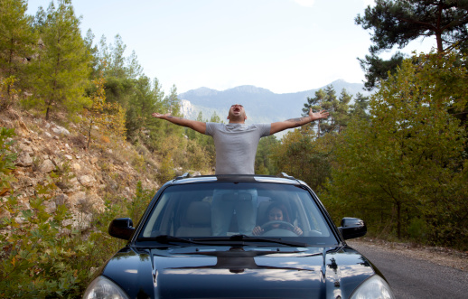 Young Man Lifting Arms Up Standing in Car Sun Roof